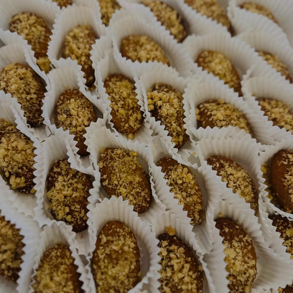Many small, nut-topped desserts arranged in white fluted paper cups.