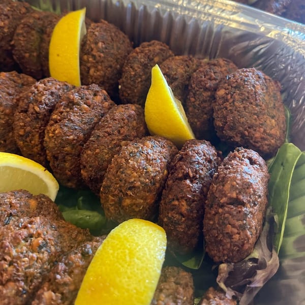 Many crispy brown falafel patties with bright lemon wedges in a silver foil tray.