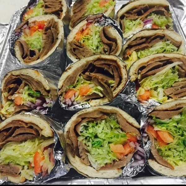 Tray of doner kebabs filled with sliced meat, fresh lettuce, tomatoes, and red onions.