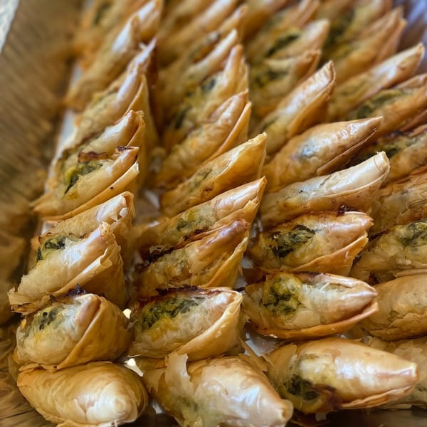 Rows of golden brown triangular pastries filled with green spinach and cheese.