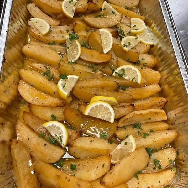 Golden roasted potato wedges in a savory sauce, garnished with lemon and parsley.